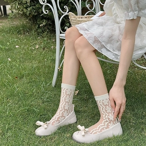 Close-up of white floral lace socks paired with sweet bow ballet flats on green grass