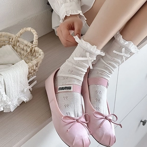 Detail of pink satin ballet flats with white lace socks and decorative bow patterns