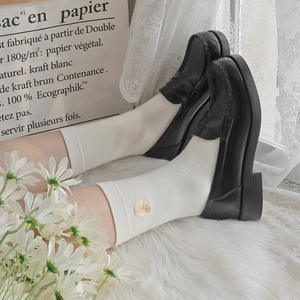 White crew socks with daisy embroidery paired with black loafers in a soft studio setting