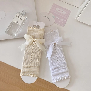 Detail of sweet white lace socks featuring silk bows and pearl accents on beige surface
