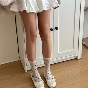 Détail de chaussettes en résille crème à pois noirs et chaussures Mary Jane blanches