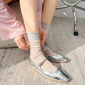 Silver ballet flats with metallic finish and sheer crew socks on a neutral woven rug