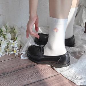 Close-up of white crew socks with pink flower embroidery paired with black loafers