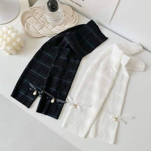 Sweet ballet style white and black knit arm warmers with pearl bow accents on white desk
