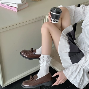 Detail of white mid-calf socks with 3D ribbon bows and brown loafers in preppy style