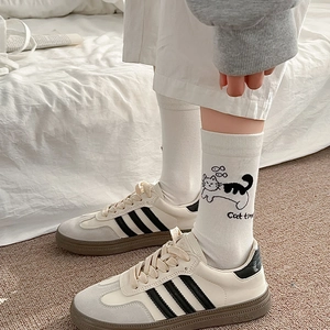 Détail de chaussettes en coton blanc imprimé chat et baskets à bandes noires contrastées