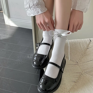 Détail de chaussettes blanches avec nœud en ruban et étoile strass sur Mary Janes noires