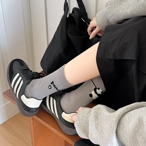 Détail de chaussettes en coton gris clair avec texte panda et empreinte avec baskets noires