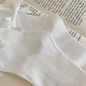 Detail of white rib-knit Lolita socks featuring a satin bow on a vintage book