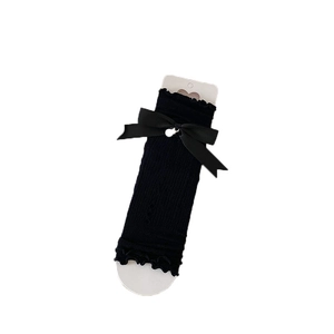 Jambières noires tricotées avec nœud en satin et perle sur support en carton blanc