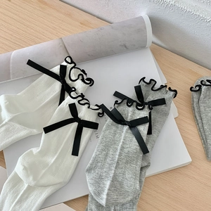 Detail of mesh socks featuring a black ribbon bow and elegant ruffled cuffs on cotton fabric