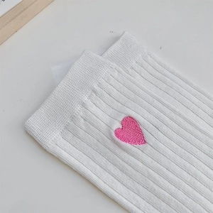 Close-up of white ribbed cotton socks featuring a delicate pink heart embroidery detail