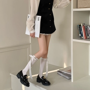 Detail of white calf socks with silk ribbon bow and black leather platform loafers
