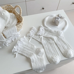 Detailed shot of white lace socks with silk bows and hollow-out mesh patterns in a gift box