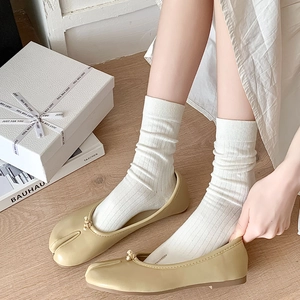 Close-up of beige Tabi flat shoes with split-toe design and ribbed cotton mid-calf socks