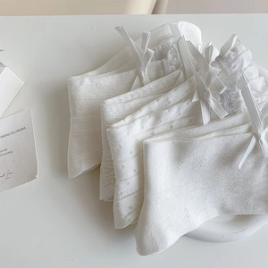 Close-up of white lace mesh socks with silk bows and ruffles on a minimalist background