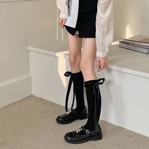 Detail of black over-the-knee socks with satin bows and pearl Mary Jane shoes