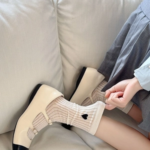 Close-up of cream striped socks with heart embroidery and Mary Jane shoes on a sofa