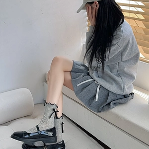 Detail of grey ruffled crew socks with black bows paired with Mary Jane shoes and pleated skirt