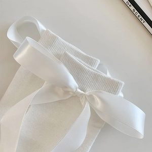 Close-up of white knitted knee-high sock featuring a large satin bow and ribbon detail