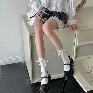 Détail de chaussettes mi-mollet blanches avec nœuds, étoiles et chaussures Mary Jane noires