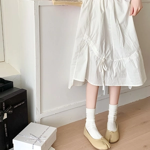 Detail of beige Tabi shoes paired with white cotton socks and a pleated linen skirt
