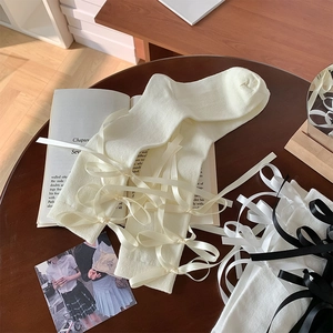Detail van crème witte Lolita kniekousen met zijden strikjes op een vintage houten tafel