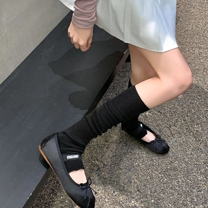 Detail shot of black ballet flats with bow and knit slouch socks on a stone path
