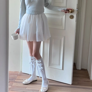Detail van witte over-the-knee sokken met satijnen strikken en balletcore tutu-rok