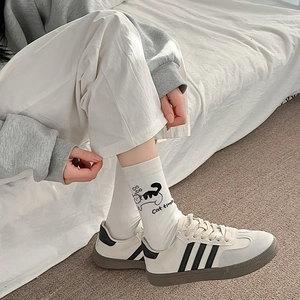 Détail de chaussettes en coton blanc avec chat illustré et baskets aux rayures noires