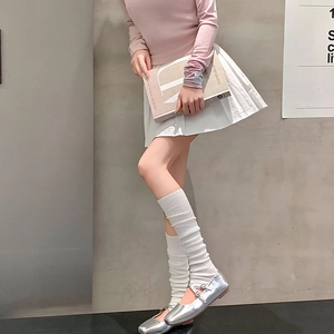 Detail of white knitted slouch socks styled with silver Mary Jane shoes and pleated skirt