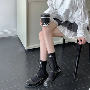 Détail de chaussettes hautes noires avec nœud en soie et breloques étoiles argentées