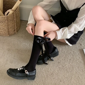 Detail of black knee-high socks with large satin bows and pearl Mary Jane shoes