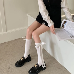 Detail of white knee-high socks featuring a large satin bow and black patent loafers