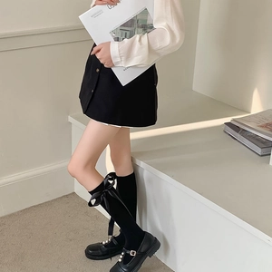 Detail of black knee-high socks featuring a large satin bow paired with Mary Jane shoes