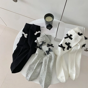 Detail of JK style ribbed socks with bow knots in black, white and grey on a white table