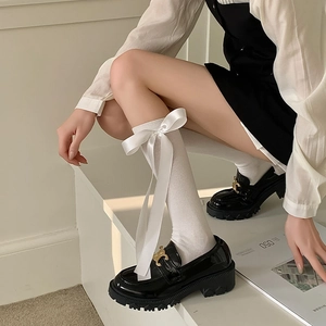 Detail of white calf-high socks featuring a large satin bow and sleek loafers
