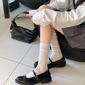 Close-up of white hollow grid socks paired with black patent leather Mary Jane shoes