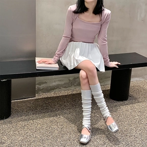 Close-up of white knitted leg warmers styled with silver Mary Jane shoes and pleated skirt