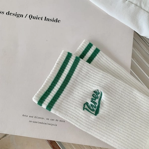 Detail of white cotton crew socks with green stripes and 'Three' letter embroidery