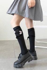 Detail of JK style black knee-high socks featuring pink butterfly embroidery and ribbon laces