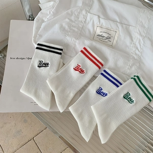 Detail view of white ribbed cotton socks featuring striped cuffs and Three embroidery