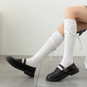 Detail of white knee-high socks featuring 3D butterfly embroidery and ribbon lace-up design