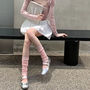 Pink ribbed calf-high leg warmers paired with silver Mary Jane shoes and pleated skirt