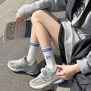 Detail of white cotton crew socks with blue stripes and Three embroidery on gray sneakers