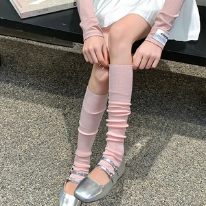 Detail of pink knitted leg warmers styled with silver Mary Jane shoes on gravel ground