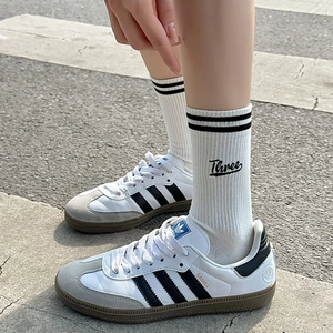 Outdoor shot of white cotton crew socks with black stripes and embroidery worn with sneakers