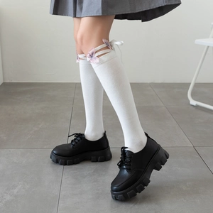 Detail of white knee-high socks featuring pink butterfly embroidery and ribbon lace-up