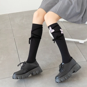 Detail of black knee-high socks featuring pink butterfly embroidery and velvet ribbon lace-up