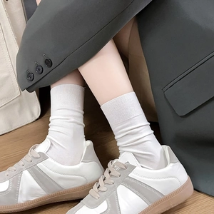 Close-up of white ribbed crew socks paired with vintage sneakers on a wooden floor